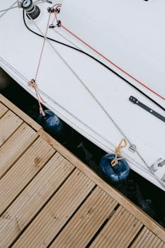 Detailed view of sailboat tied to a wooden dock, showcasing nautical ropes and equipment.