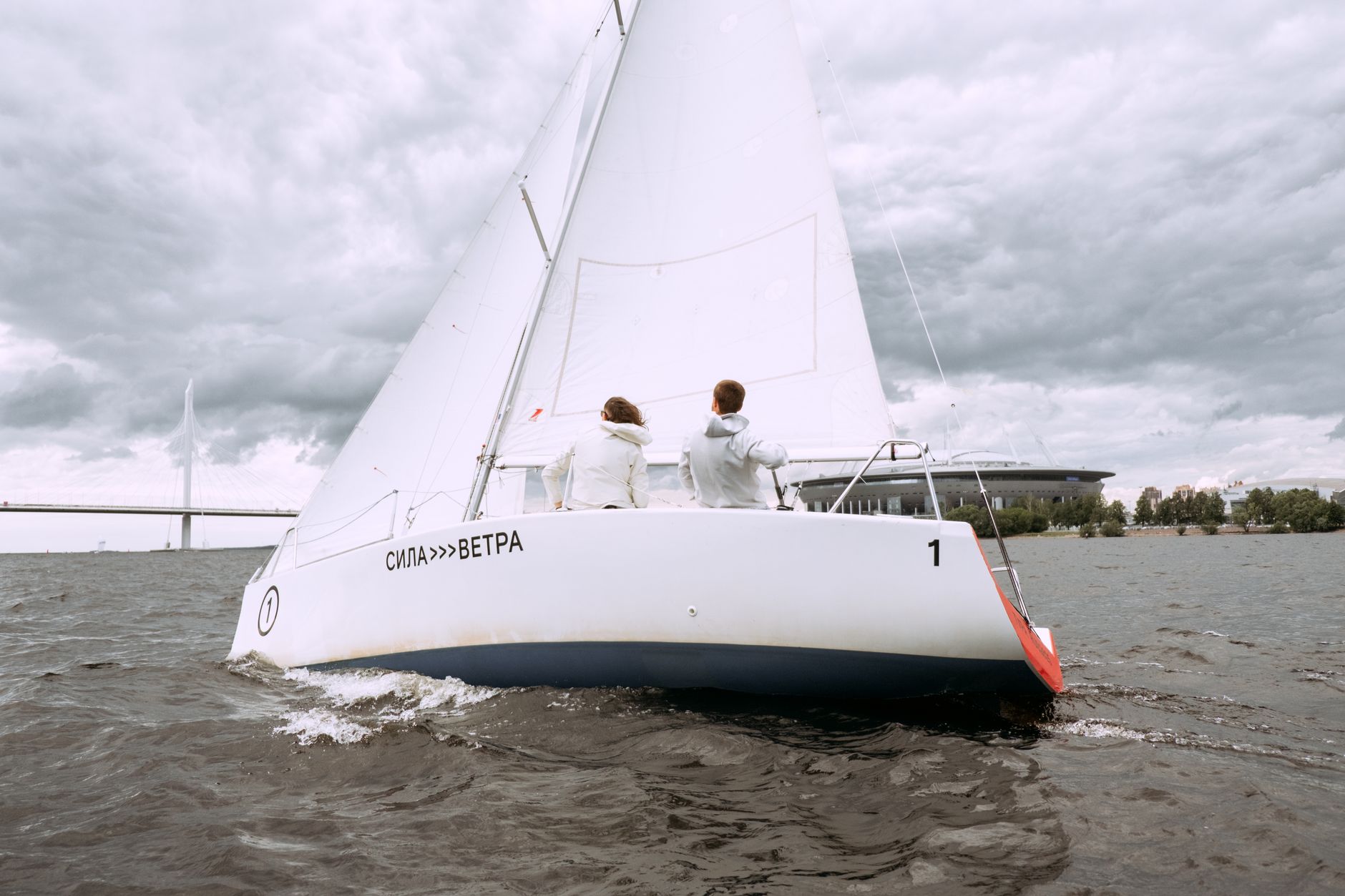 Two people sailing a yacht on a cloudy day, embracing adventure on open water.