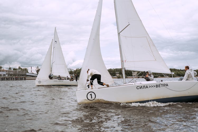 Person In White Sail Boat On Body Of Water