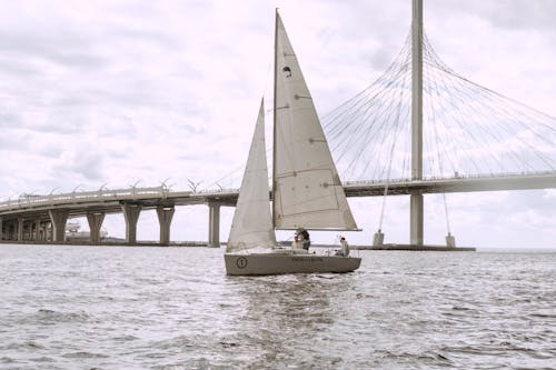 Grayscale Photo of Person Riding on Boat on Sea Near Bridge