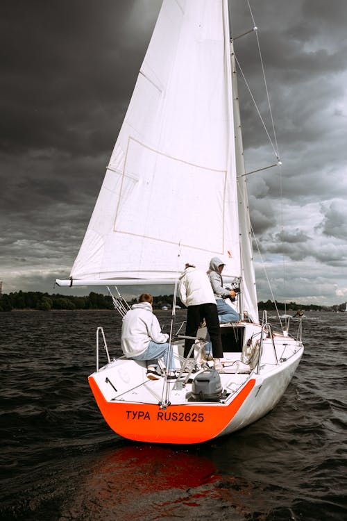 Man in White Shirt and Black Pants Riding on Orange and White Sailboat on Sea during