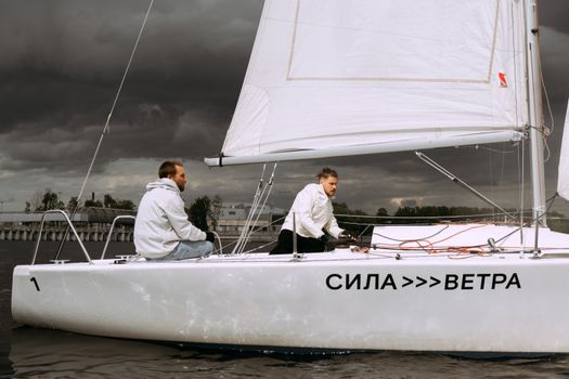 Two men sailing a yacht under stormy skies, showcasing teamwork and adventure.