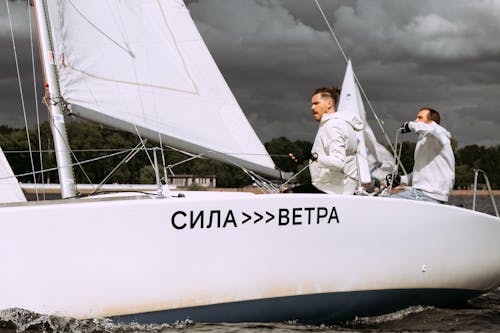 Man In Wit Shirt Met Lange Mouwen En Zwarte Broek, Zittend Op Een Witte Zeilboot