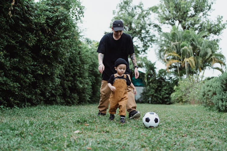 Father Playing Ball With Son On Grass