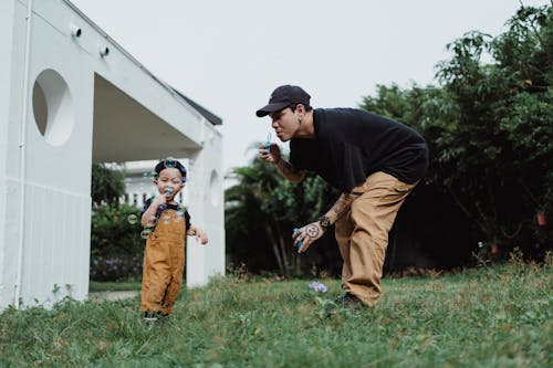 Man in Black T-Shirt and Little Boy Blowing Soap Bubbles