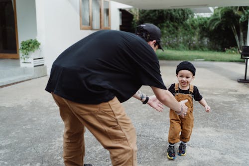 Man in Black T-shirt Reaching Out to Little Boy in Brown Pants