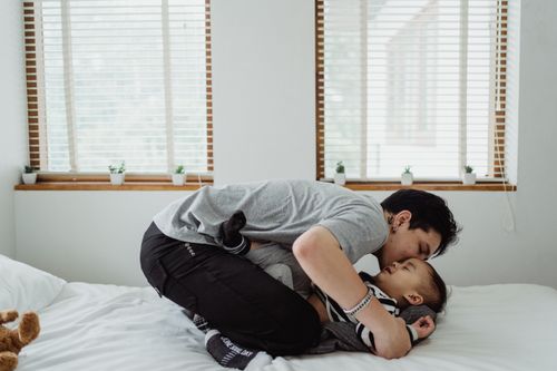 Free Father lovingly embraces child on bed, capturing a tender family moment indoors with natural light. Stock Photo