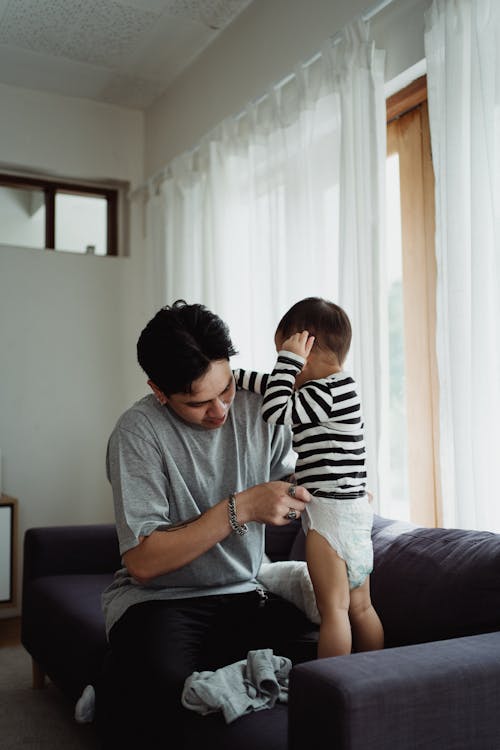 Free Father Dressing up Baby Son in Living Room Stock Photo