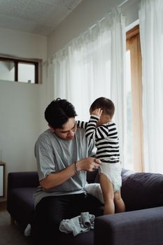 在自然光线舒适的客厅里，一位父亲帮他的小儿子穿好衣服