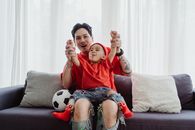 父亲和儿子穿着红色衣服，坐在沙发上，在室内享受游戏时间