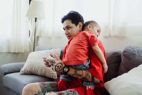 Free A man and his child share a moment while playing video games on the couch at home. Stock Photo