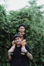 Portrait of a Man Carrying Son on Shoulders with Bush in Background