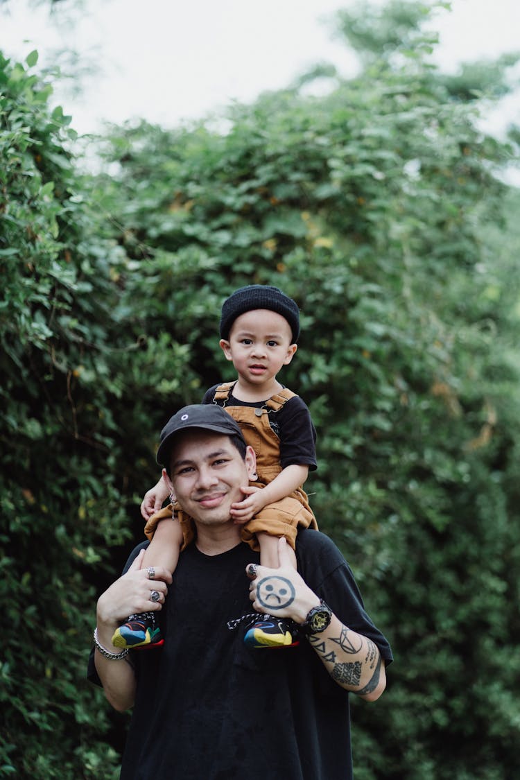 Portrait Of A Man Carrying Son On Shoulders With Bush In Background