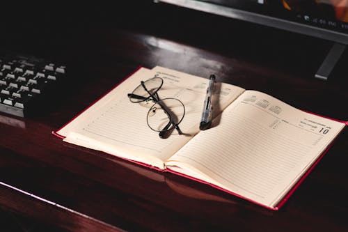 Black Framed Eyeglasses and Pen on Top of a Notebook