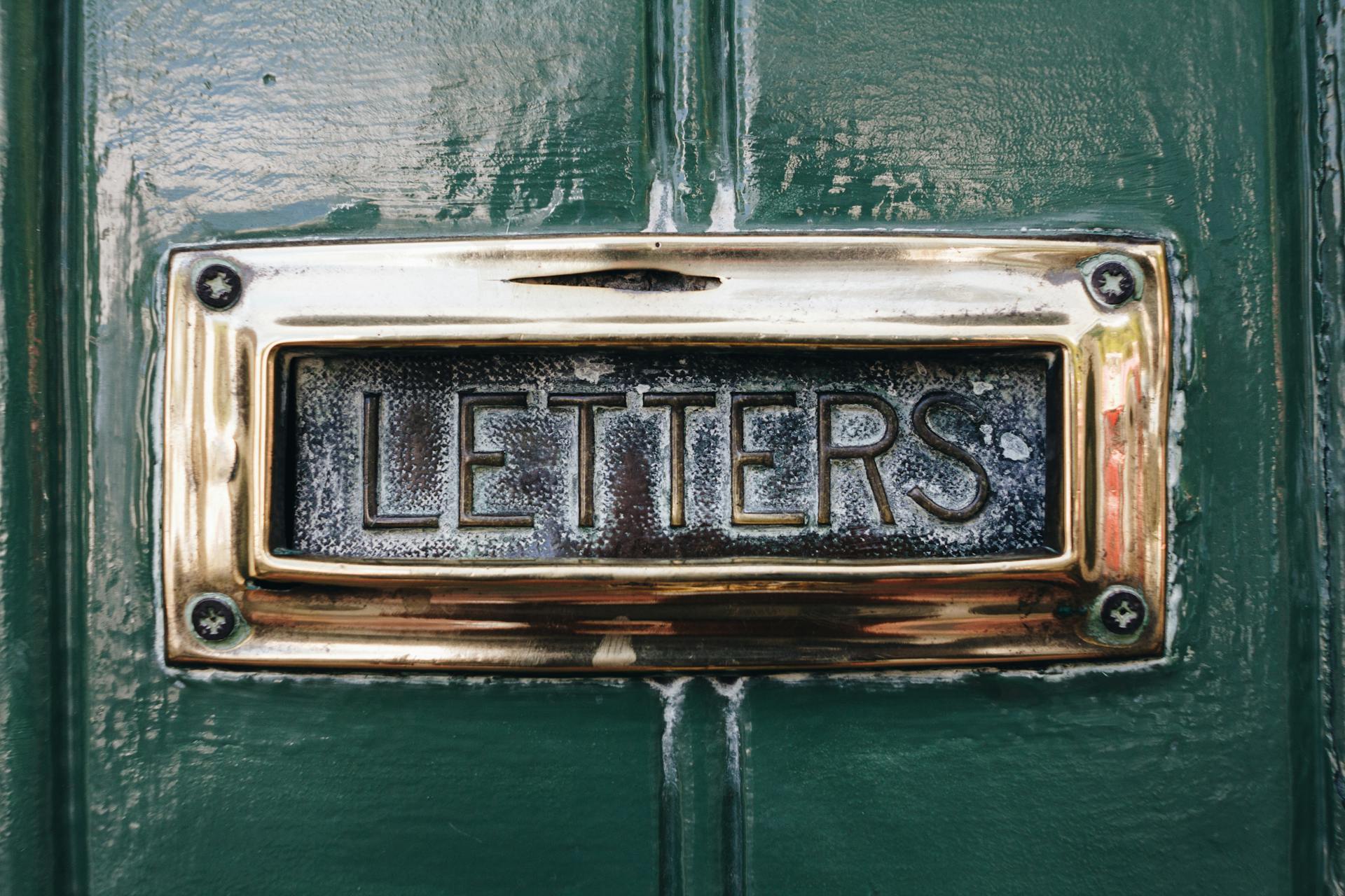 Close-up of an antique mail slot labeled 'letters' on a painted green door.