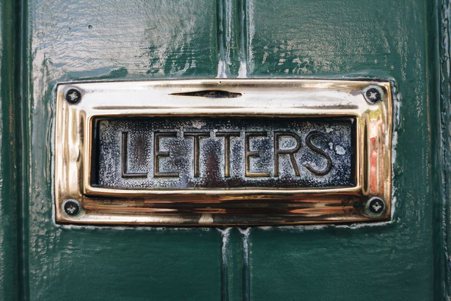 A brass letterbox marked letters on a dark door