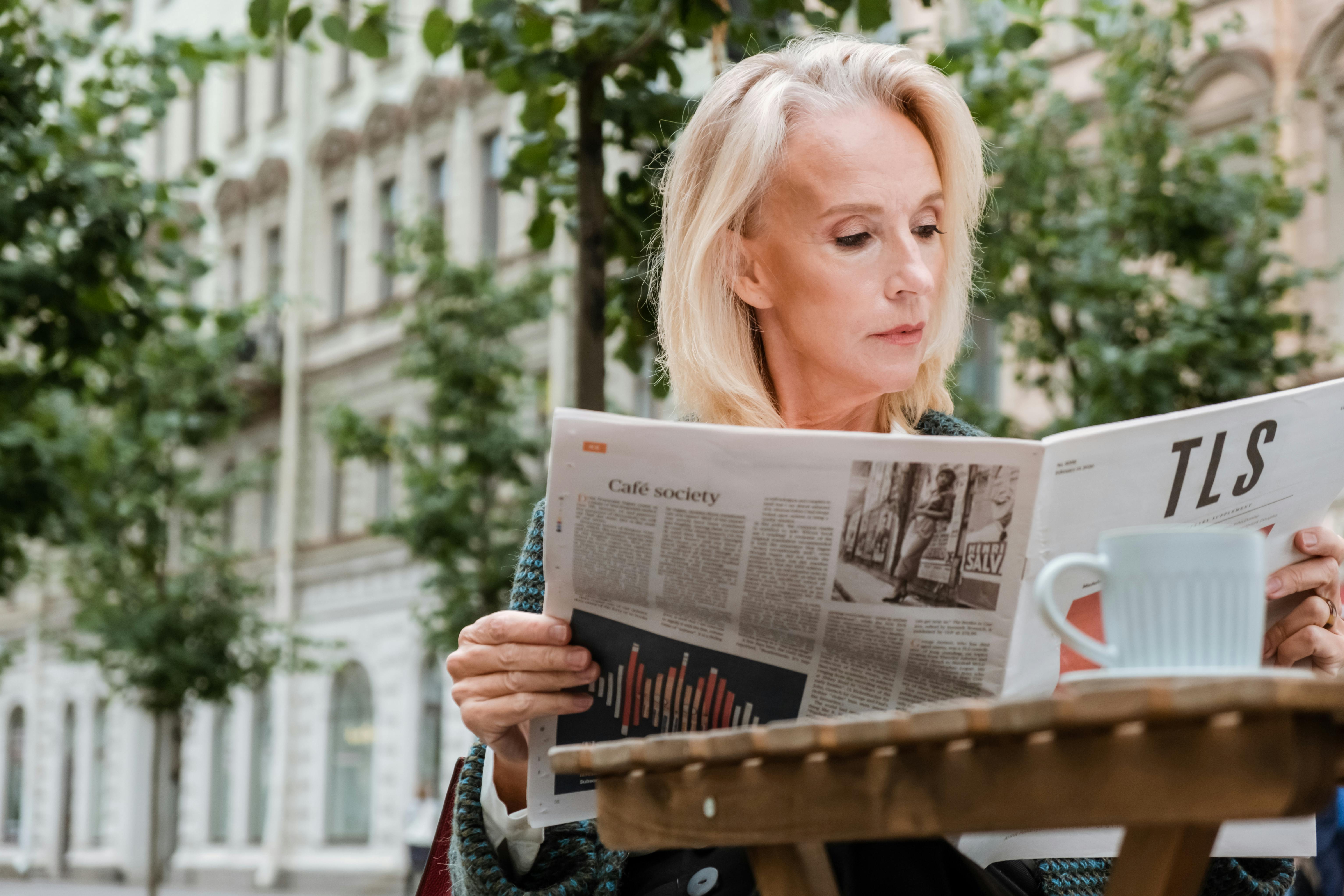 woman reading newspaper on brown wooden bench