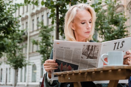 Mature woman enjoying summer morning reading newspaper at an outdoor cafe in Saint Petersburg.