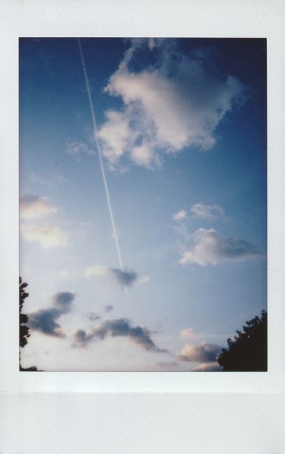 A polaroid photo capturing a blue sky with fluffy clouds and a vapor trail, evoking tranquility.
