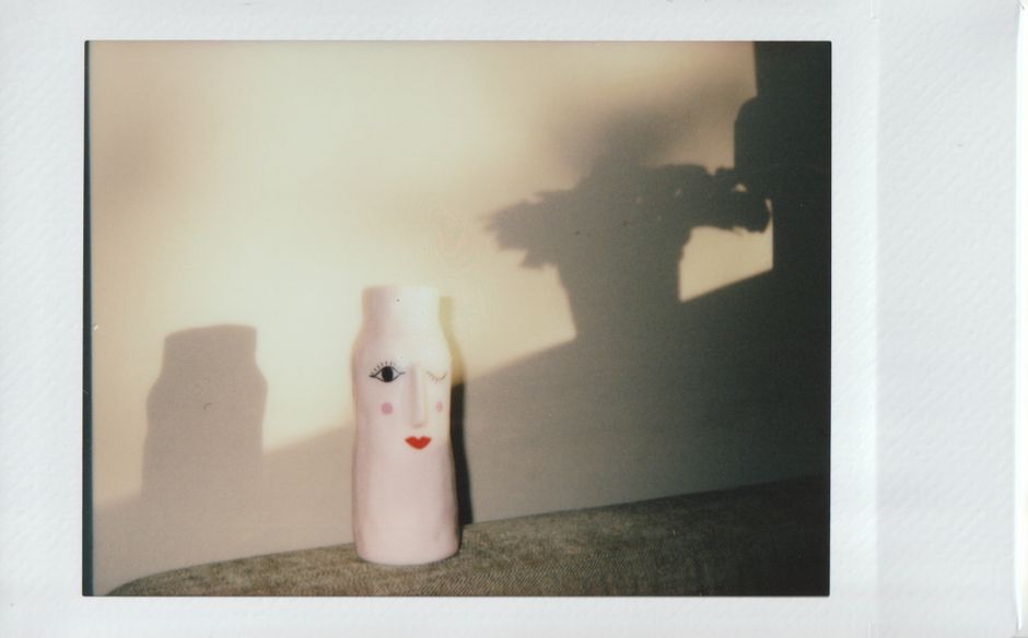 Artistic vase with face design casting shadow on wall, bathed in warm light.