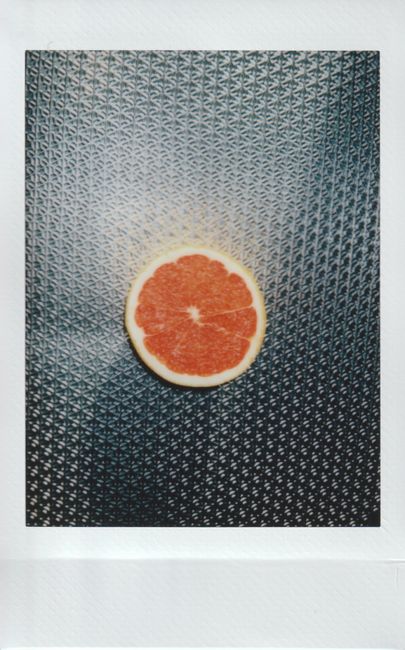 A vibrant grapefruit slice placed on a unique metal surface, creatively shot in instant film style.