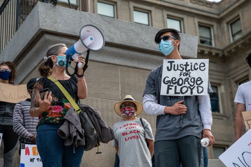 Free Low angle of unrecognizable social justice warriors in masks with placards and loudspeaker during strike near building Stock Photo