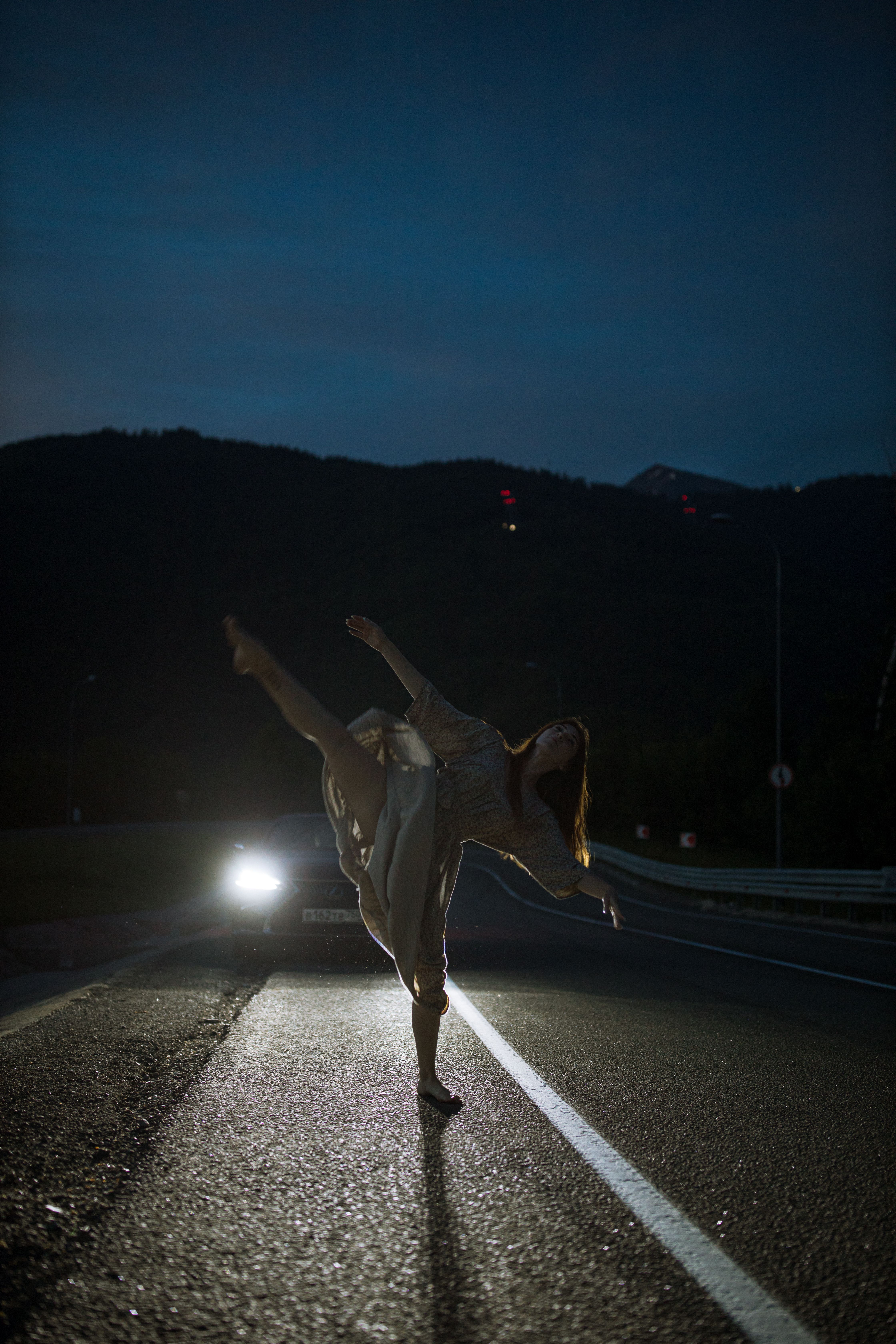 夜晚，空旷的道路上，一位女舞者在车灯的照耀下优雅起舞