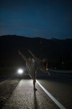 夜晚，空旷的道路上，一位女舞者在车灯的照耀下优雅起舞