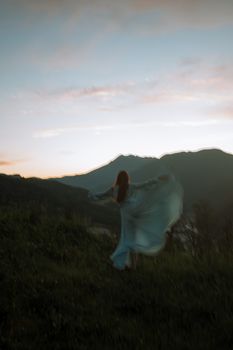 一位无法辨认的女人在草山上优雅地旋转，背景是高山