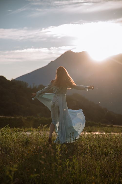 Free A woman in a blue dress spins gracefully in a mountain meadow at sunset. Stock Photo