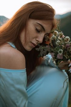 一个红发女人安静地闭着眼睛，在户外捧着一束野花