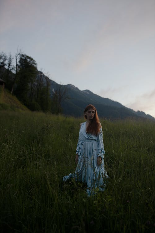 Woman in Blue Dress Standing on Green Grass in the Mountains