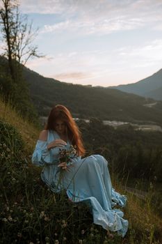 日落时分，一位穿着蓝色连衣裙的女人在宁静的山景中手持鲜花