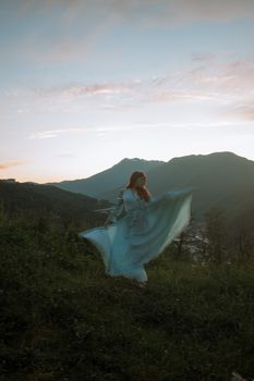 黄昏时分，一位红发女人穿着蓝色连衣裙，优雅地站在风景秀丽的山区中