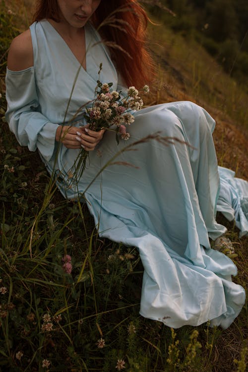 Free Person in a Dress Sitting on Grass Holding Bouquet of Flowers Stock Photo