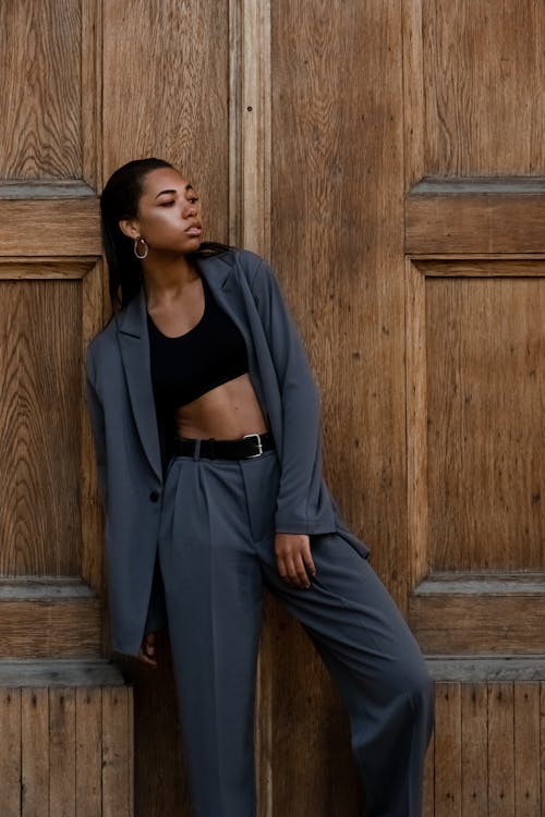 Woman in Black Long Sleeve Shirt and Blue Pants Standing Beside Brown Wooden Wall