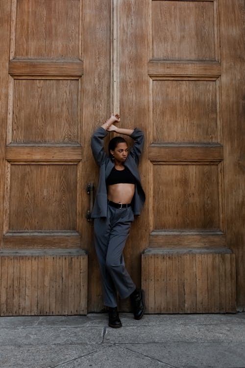 Woman in Black Tank Top and Blue Denim Jeans Standing Beside Brown Wooden Door