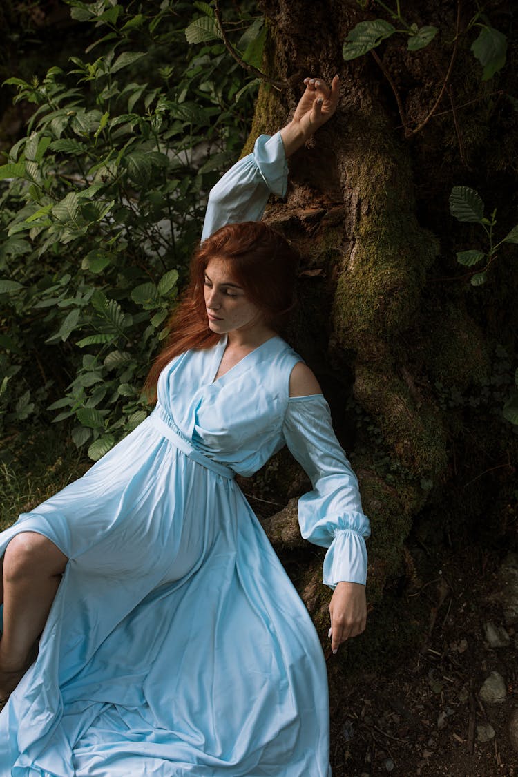 Woman In Light Blue Dress Leaning On Tree Trunk