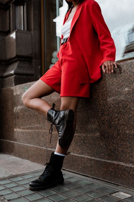 Fashionable woman in a bold red suit and boots posing against classic architecture in the city.
