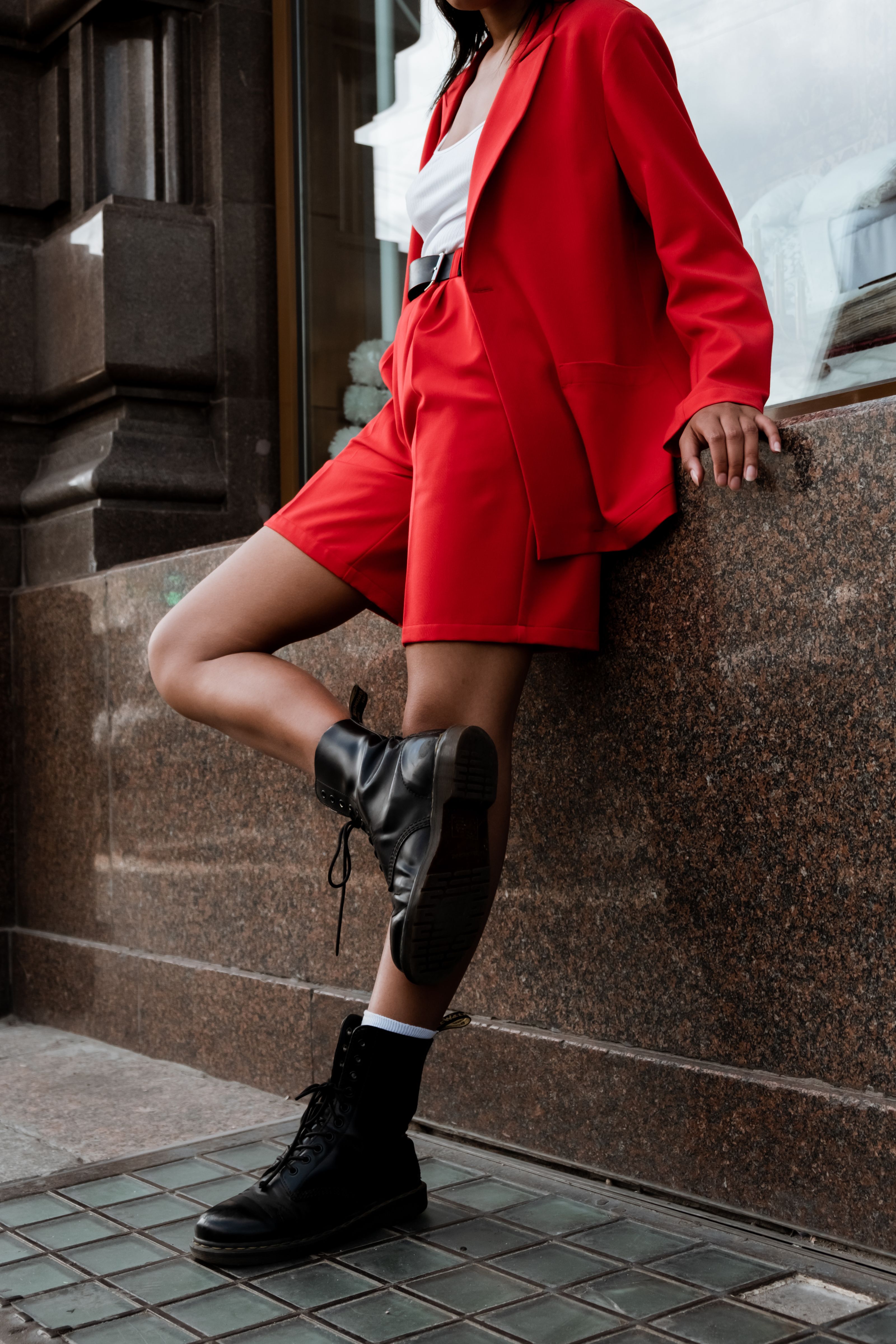 Mulher fashionista em um ousado conjunto vermelho e botas posando em frente à arquitetura clássica da cidade.