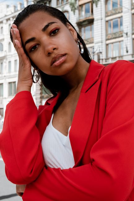 Elegant outdoor portrait of a woman in a red suit, exuding confidence and fashion on a city street.