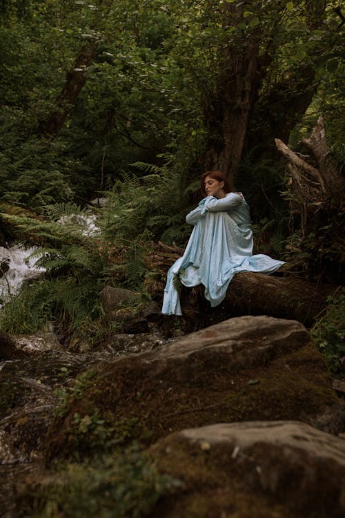 Woman in a Blue Dress Sitting in the Middle of a Forest