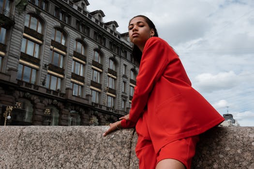 Stylish woman in red suit posing with historic architecture background, exuding confidence.