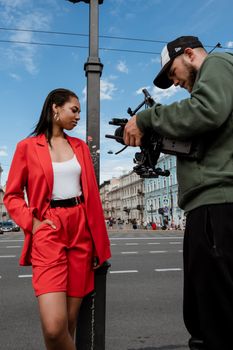 Model in a red suit and cameraman in urban setting, capturing fashion.