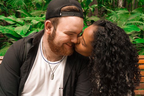 Photo of a Woman Kissing a Man with a Black Cap