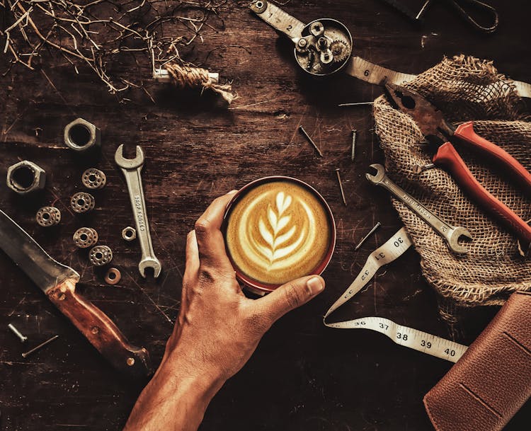 Overhead Shot Of A Person Holding A Cup Of Coffee Near Tools