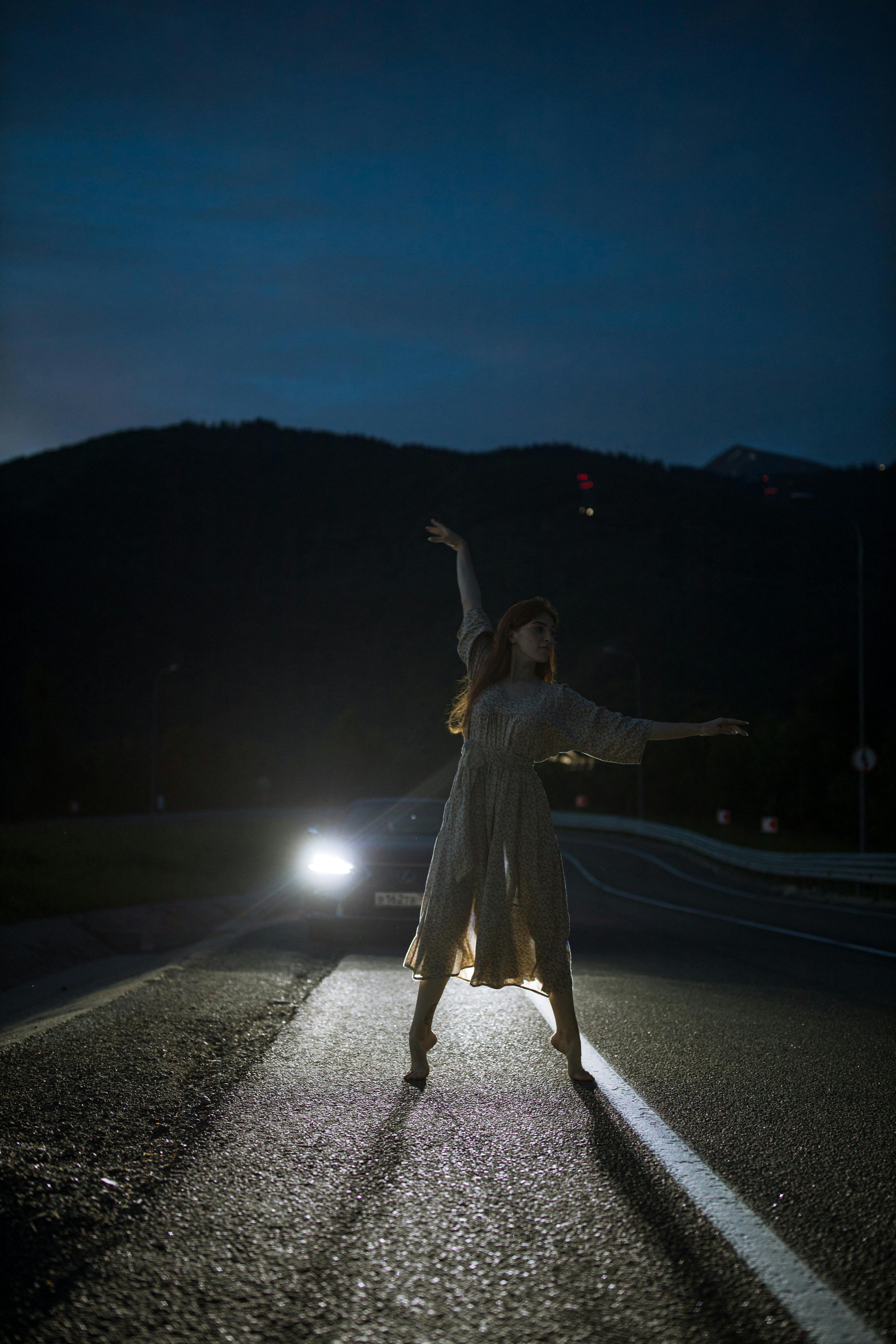 photo of a woman dancing on a road during the night