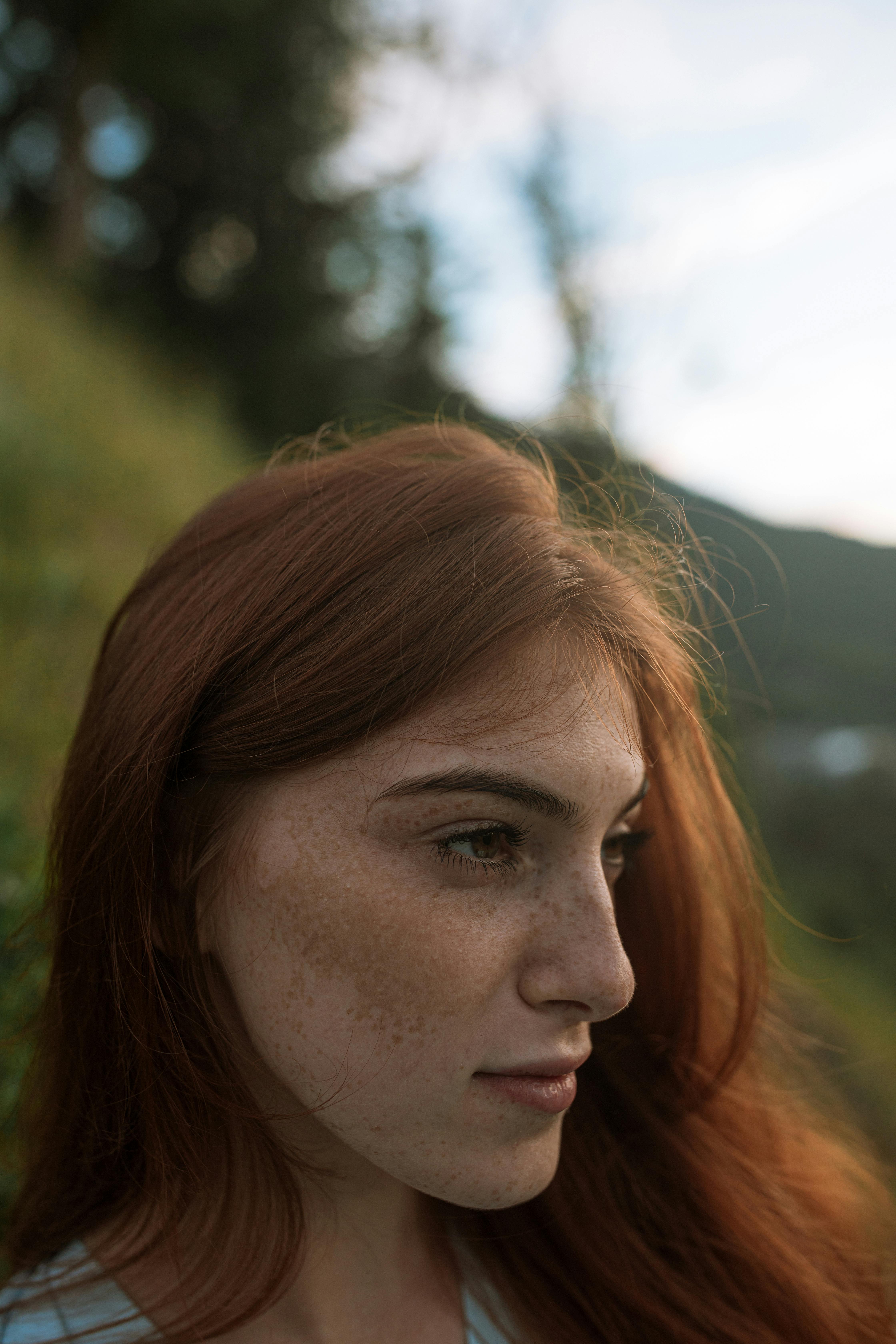 Close-up portrait of a freckled woman with red hair outdoors, exuding natural beauty and serenity.
