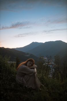 暮色中，一位红发女子坐在风景秀丽的草山上，显得格外宁静