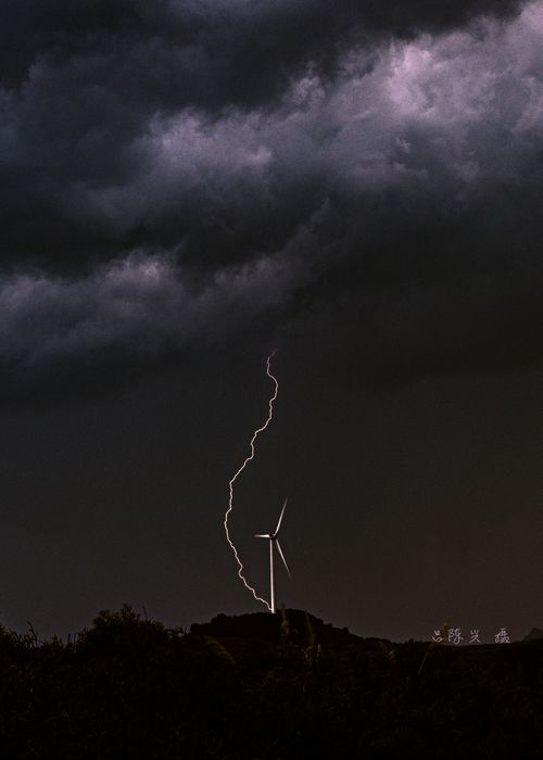 Free Lightning strikes near a wind turbine under a stormy sky, symbolizing the power of renewable energy. Stock Photo
